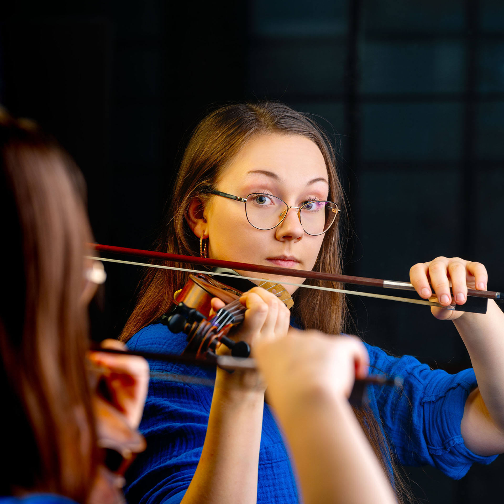Siniseen paitaan pukeutunut nais viulisti katsoo peilin kautta suoraan kameraan.